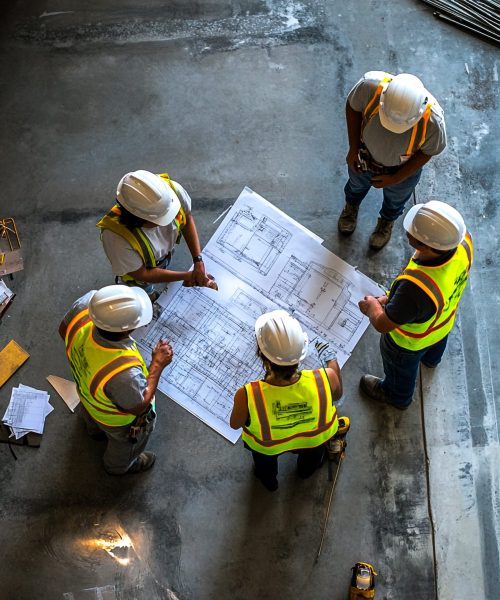 Diverse Team of Engineers and Construction Workers Collaborating on Project Plans at Industrial Site