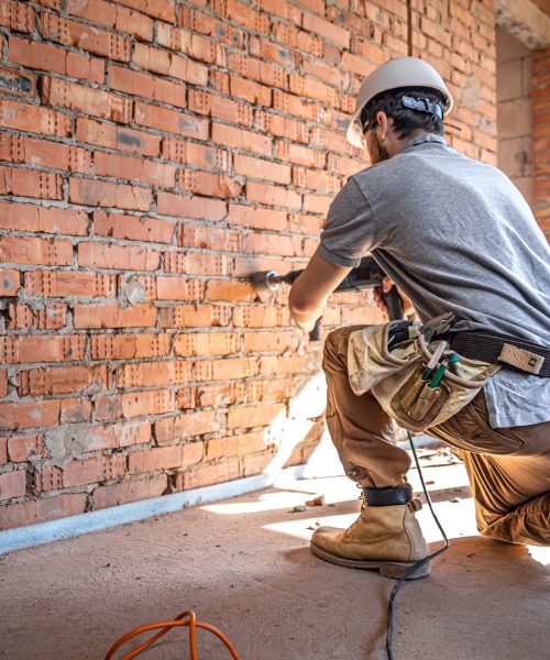 Handyman at a construction site in the process of drilling a wall with a perforator.
